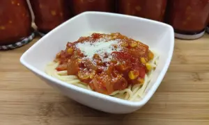 Porcja spaghetti z sosem buffalo, posypana parmezanem. W tle słoiki z domowym sosem.