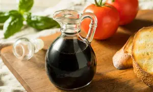 Szklana karafka z ciemnym, gęstym **sosem balsamicznym** obok pomidorów, bazylii i grzanek na desce.
