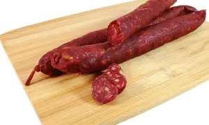 Trzy długie kiełbaski chorizo leżą na drewnianej desce. Jedna jest przekrojona, ukazując charakterystyczne kawałki mięsa i tłuszczu.