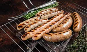 Aromatyczna biała kiełbasa z grilla, rumiana i soczysta, z ziołami i widelcem do serwowania.