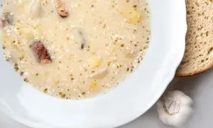 Aksamitny zakwas na barszcz biały z kawałkami kiełbasy, ziemniaków i czosnkiem. Obok kromka chleba.