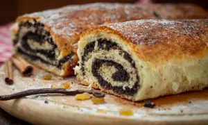 Pyszny makowiec który zawsze się udaje, z bogatym nadzieniem makowym, posypany cukrem pudrem. Obok leżą laski cynamonu i wanilii.