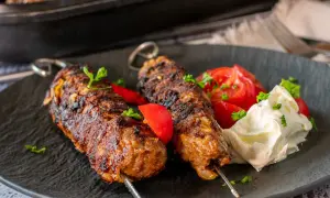 Dwa soczyste kofta kebab na patyczkach, podane z pomidorami i kremowym sosem.