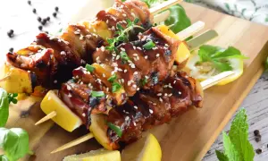 Aromatyczne yakitori z kurczaka w sosie teriyaki, posypane sezamem i szczypiorkiem, podane z cytryną na drewnianej desce.