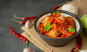 Miseczka pełna pikantnego, czerwonego kimchi, z suszonymi papryczkami chili i czosnkiem w tle. To tradycyjne koreańskie danie, które warto poznać!
