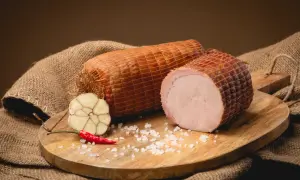 Dwie wędzone szynki na desce, obok czosnek, papryczka chili i sól. Idealne składniki, by dowiedzieć się, jak wędzić szynkę.