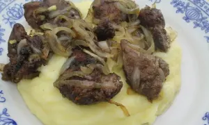 Pyszna wątróbka drobiowa z cebulką na kremowym purée ziemniaczanym, podana na talerzu z niebieskim wzorem.
