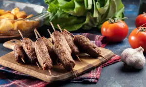 Aksamitne ćevapi na drewnianej desce, obok pomidory, czosnek i pieczone ziemniaki.
