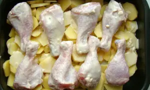 Pałki kurczaka w sosie, ułożone na ziemniakach w naczyniu żaroodpornym. Idealne do pieczenia, by uzyskać chrupiące danie.