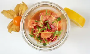 Pyszne ceviche z łososia w szklanym naczyniu, ozdobione świeżymi ziołami, z cytryną i physalis w tle.