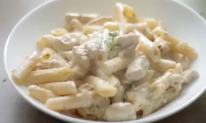 Penne z kurczakiem w kremowym sosie śmietanowym, udekorowane gałązką ziół. Pyszne danie gotowe do podania.