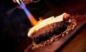 Gorący piesek w czarnej bułce z sezamem, topiony ser i płomienie od palnika – efektowne flambirowanie.