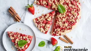 Pyszna tarta z truskawkami i kruszonką, ozdobiona miętą, obok laski cynamonu i świeżych truskawek. Idealna na letnie popołudnie.