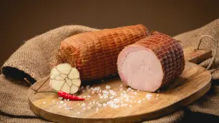 Dwie wędzone szynki na desce, obok czosnek, papryczka chili i sól. Idealne składniki, by dowiedzieć się, jak wędzić szynkę.
