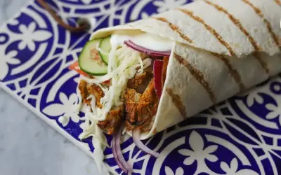 Pyszny kebab w picie z soczystym mięsem, chrupiącą surówką, pomidorem, ogórkiem i czerwoną cebulą, zawinięty w ciepły placek.