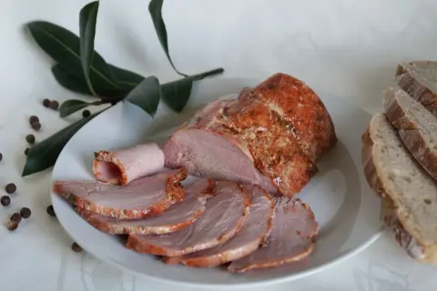 Soczysta kiełbasa z łopatki z szynkowara, pokrojona w plastry, podana z chlebem i liśćmi laurowymi.