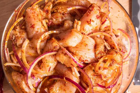 Kawałki kurczaka w misce z czerwoną cebulą i przyprawami, gotowe na grill. Ta marynata do kurczaka na grilla zapowiada pyszne danie.
