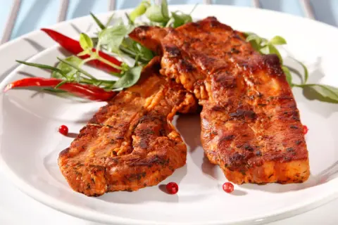 Grillowany boczek w aromatycznej marynacie, podany z papryczkami chili i zielonymi ziołami. Idealny na letnie przyjęcie.