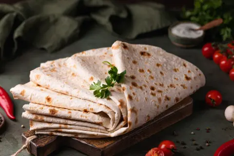 Stos cienkiego, puszystego lawaszu, ozdobiony natką pietruszki, obok pomidorków, papryczki chili i pieprzu. Idealny do wrapów.