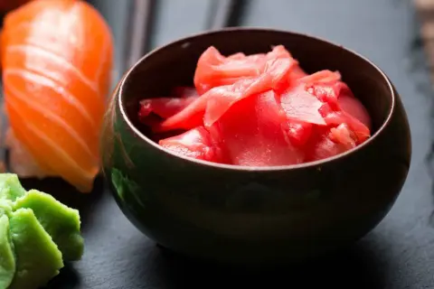 Miseczka z różowym, marynowanym imbirem obok sushi i wasabi. Idealny dodatek do japońskich potraw.