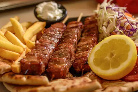 Pyszne souvlaki na patykach, podane z frytkami, pitą, sałatką i cytryną.