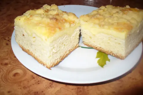 Puszyste ciasto drożdżowe z serem, z kruszonką na wierzchu, pokrojone na dwa kawałki na białym talerzu.