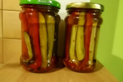Dwa słoiki domowych pikli z ogórków słodko-kwaśnych, z dodatkiem czerwonej papryki.