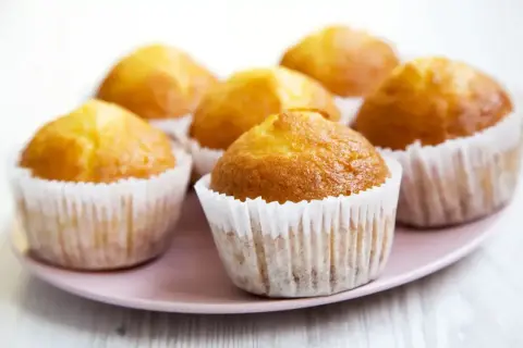 Idealny przepis na wilgotne i puszyste muffinki. Złociste, pachnące babeczki na różowym talerzu.