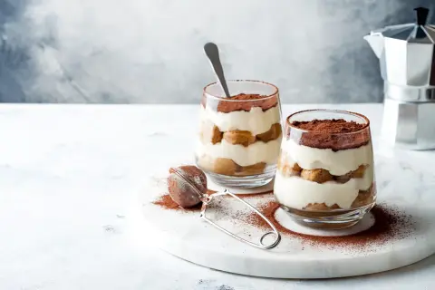 Dwa pucharki z kremowym, warstwowym deserem, posypane kakao. To najprostsze tiramisu, idealne na deser.