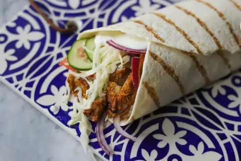 Pyszny kebab w picie z soczystym mięsem, chrupiącą surówką, pomidorem, ogórkiem i czerwoną cebulą, zawinięty w ciepły placek.