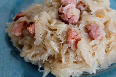 Kapusta kiszona zasmażana z boczkiem, podana na talerzu. Aromatyczne danie, które rozpływa się w ustach.