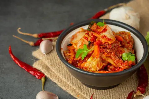 Miseczka pełna pikantnego, czerwonego kimchi, z suszonymi papryczkami chili i czosnkiem w tle. To tradycyjne koreańskie danie, które warto poznać!