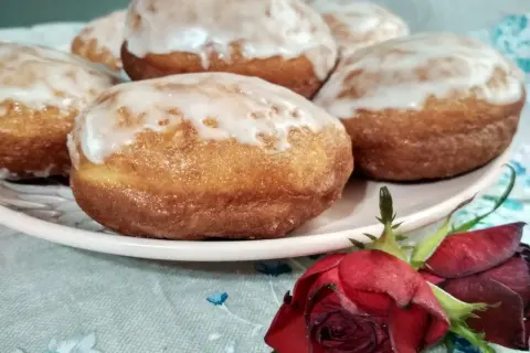 Pączki z ziemniakami Ewy Wachowicz, oblane lukrem, kuszą na talerzu. Obok leży czerwona róża.