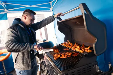 Mężczyzna przygotowuje pyszne skrzydełka i mięso na grillu. Idealne grillowanie w słoneczny dzień.
