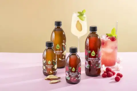 Butelki kombuchy imbirowej i malinowo-hibiskusowej, obok drinków z malinami i imbirem. To jest kombucha co to za napój?
