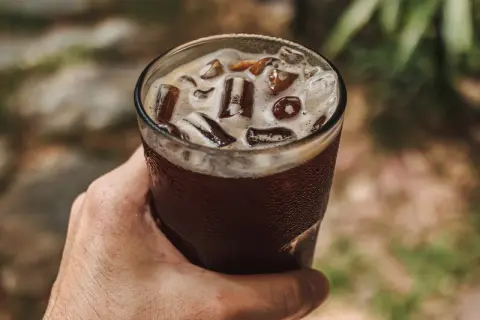 Dłoń trzyma szklankę orzeźwiającego napoju z lodem. To idealny sposób na ochłodę, gdy zastanawiasz się, cold brew co to.
