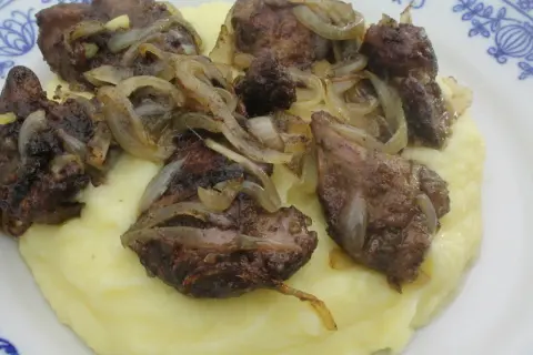 Pyszna wątróbka drobiowa z cebulką na kremowym purée ziemniaczanym, podana na talerzu z niebieskim wzorem.