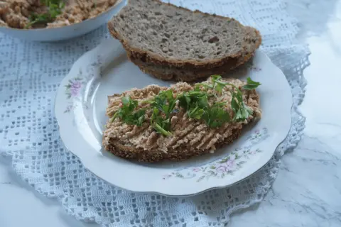 Na talerzu z różanym wzorem leży kromka ciemnego chleba z pastą jajeczną i natką pietruszki. Obok druga kromka, a w tle miseczka z pastą. Taka pyszna awanturka na śniadanie!