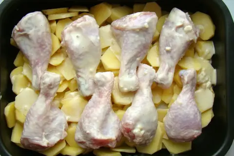Pałki kurczaka w sosie, ułożone na ziemniakach w naczyniu żaroodpornym. Idealne do pieczenia, by uzyskać chrupiące danie.