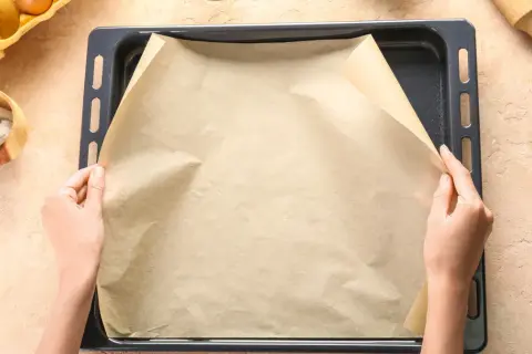 Dłonie rozkładają papier do pieczenia na blasze. To świetne rozwiązanie, co zamiast papieru do pieczenia, gdy chcesz uniknąć przypalenia.
