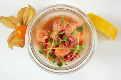 Pyszne ceviche z łososia w szklanym naczyniu, ozdobione świeżymi ziołami, z cytryną i physalis w tle.