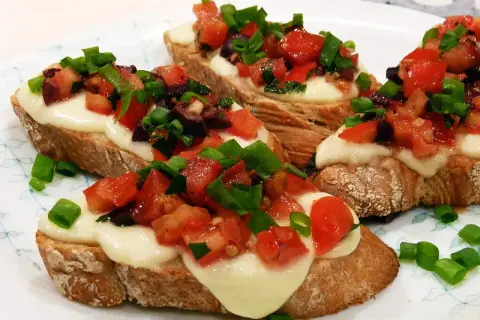Bruschetta z pomidorami i mozzarellą: chrupiące grzanki z roztopionym serem, świeżymi pomidorami, oliwkami i szczypiorkiem. Idealny przepis na szybką przekąskę.