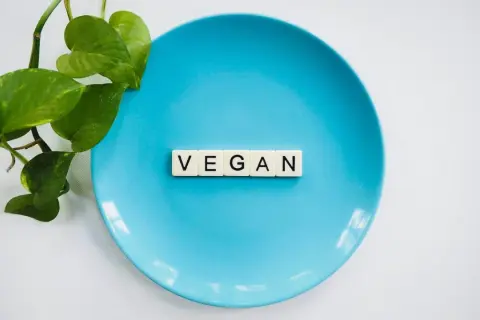 Niebieski talerz z literami "VEGAN" i zielonymi liśćmi. To symbol tego, co to jest weganizm: dieta bez produktów odzwierzęcych.