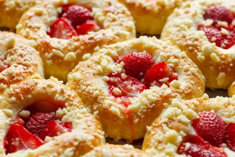 Pyszne drożdżówki z truskawkami, posypane kruszonką, kuszą swoim wyglądem i zapachem.