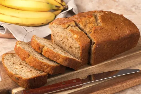 Pokrojony, złocisty chlebek bananowy, obok pęk dojrzałych bananów. Idealny na najprostszy chlebek bananowy.
