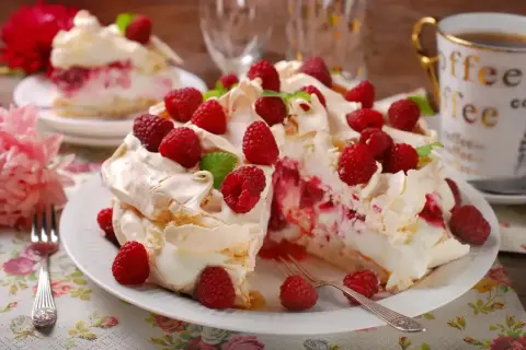 Pyszny tort bezowy z mascarpone i bitą śmietaną, ozdobiony malinami. Idealny na deser!