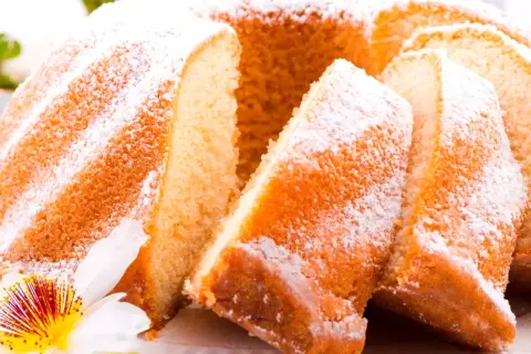 Szybka babka wilgotna, oprószona cukrem pudrem, z widocznymi kawałkami ciasta i ozdobiona kwiatem.