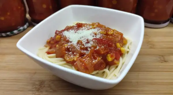 Porcja spaghetti z sosem buffalo, posypana parmezanem. W tle słoiki z domowym sosem.