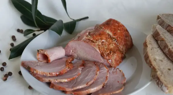 Soczysta kiełbasa z łopatki z szynkowara, pokrojona w plastry, podana z chlebem i liśćmi laurowymi.