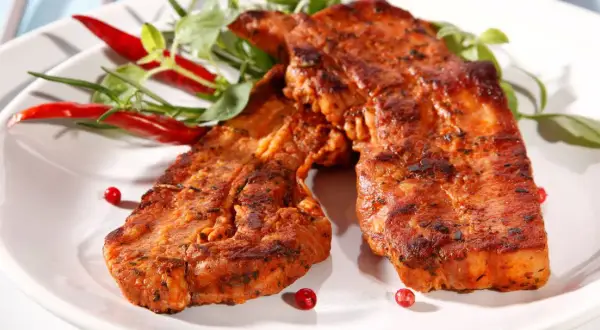 Grillowany boczek w aromatycznej marynacie, podany z papryczkami chili i zielonymi ziołami. Idealny na letnie przyjęcie.